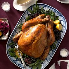 a roasted turkey on a platter with grapes, lemons and other holiday foods