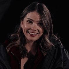 a woman smiling while sitting down in front of a black background with her hands on her chest