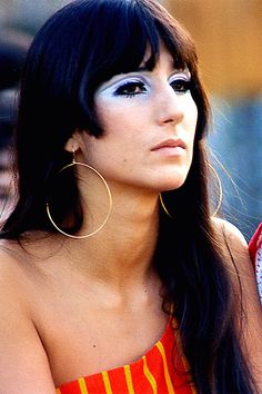 a woman with long black hair wearing large gold hoop earrings and a red striped top