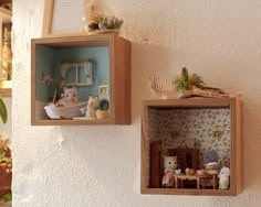 two wooden shelves with miniature figurines in them on the wall next to a potted plant