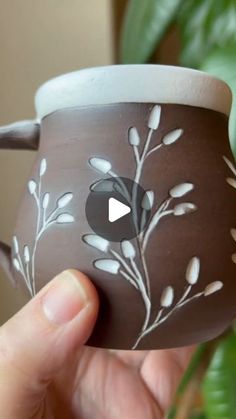 a hand holding a coffee cup with white flowers painted on the outside and inside it