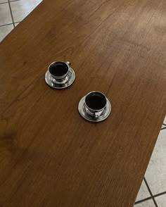 two coffee cups sitting on top of a wooden table next to a tile floor in a kitchen