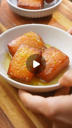 someone is holding a bowl with food in it on a wooden table next to another bowl