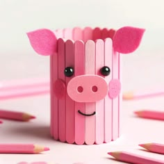 a pig made out of pencils sitting on top of a white table next to pink crayons