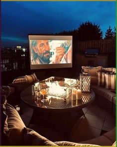 an outdoor movie screen with candles on the table and two couches in front of it