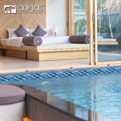 an indoor swimming pool next to a bed with pillows on it and a bench in the middle