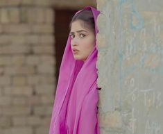 a woman wearing a pink scarf leaning against a wall