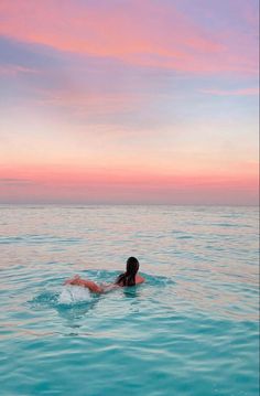 a woman swimming in the ocean at sunset or dawn with her back turned to the camera