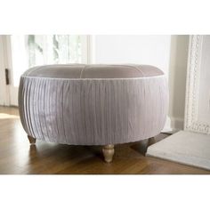 a round ottoman sitting on top of a hard wood floor next to a white fireplace