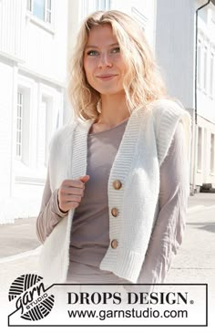 a woman standing in front of a building wearing a white cardigan sweater and jeans