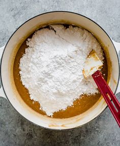 a red spatula in a pot filled with powdered sugar and other ingredients on a table