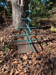 a metal sculpture sitting next to a tree on top of leaf covered ground in the woods