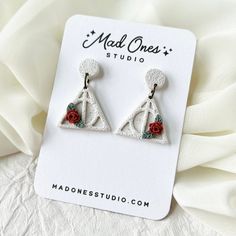 a pair of earrings with roses on them sitting on top of a white card board