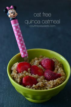 a green bowl filled with oatmeal topped with strawberries and a minnie mouse stick