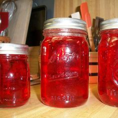 three jars with red liquid sitting on top of a wooden table