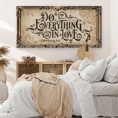 a bed with white sheets and pillows in a room next to a wooden sign that says do everything in love