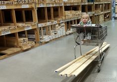 a small child sitting in a shopping cart on top of a wooden bench next to shelves