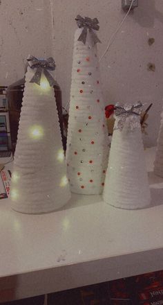 three white christmas trees with lights on them are sitting on a table next to a cd player