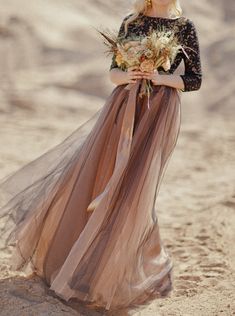 a woman standing in the sand wearing a dress with flowers on it's waist