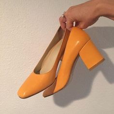 a person is holding an orange pair of high heeled shoes in their left hand