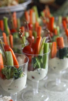 small cups filled with vegetables and dips on a white tablecloth covered table cloth