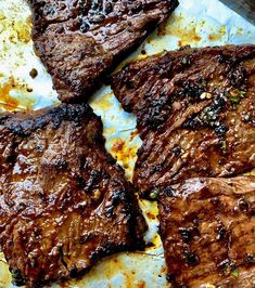 four pieces of steak sitting on top of a pan covered in sauce and seasoning