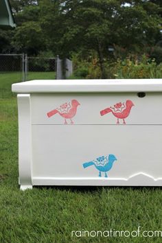 a white box with red and blue birds painted on the side sitting in some grass