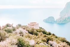 an old tower on the side of a cliff overlooking water and land with trees around it