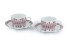 two coffee cups and saucers with designs on the rims, one is pink