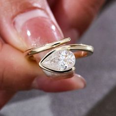 a close up of a person holding a ring with a pear shaped diamond in it