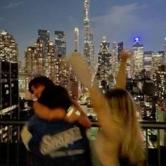 two people standing in front of a cityscape at night with their arms up