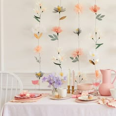 a table topped with plates and flowers next to a vase filled with pink, white and yellow flowers