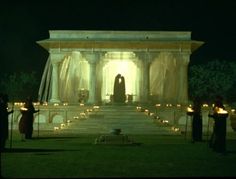 people standing in front of a building with candles lit on the ground and statues behind them