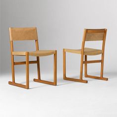 two wooden chairs sitting next to each other on a white surface with one chair facing the other