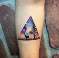 a small triangle tattoo with a deer in the woods and stars on it's side