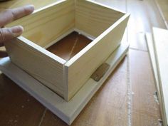 a person holding a wooden box on top of a hard wood flooring area with one hand