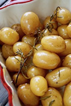 a white bowl filled with lots of small yellow potatoes next to a red and white striped napkin