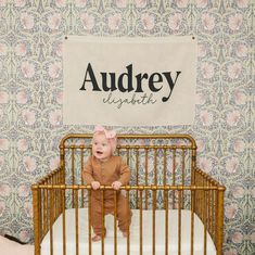 a baby sitting in a crib with a name sign above it