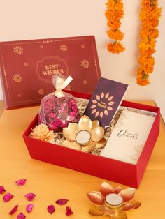 a red box filled with lots of different items next to some flowers and candles on a table