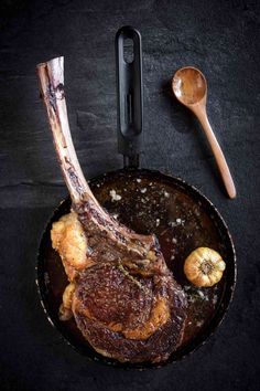 a piece of meat in a frying pan next to a spoon