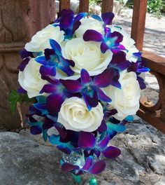 a bouquet of white and blue flowers in a vase on a stone floor next to a fence