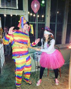 a man and woman dressed up as clowns in front of a table with balloons