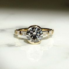 a close up of a diamond ring on a white surface with light shining in the background