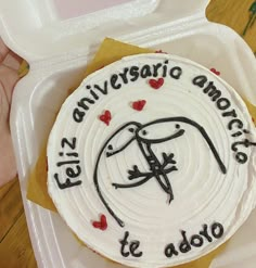 a white cake with red and black icing in a plastic container on a table