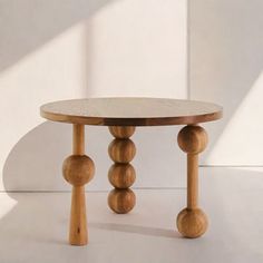 a round table with three wooden balls on the top and two legs, in front of a white wall