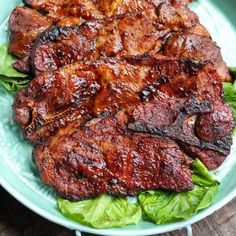 a plate with meat and lettuce on it sitting on top of a wooden table