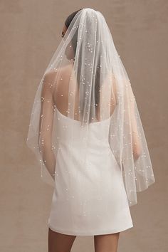 the back of a bride's wedding veil with white pearls on it and her dress