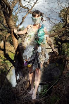 a woman wearing a face mask and dress walking through the woods with trees in the background