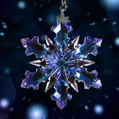 a snowflake ornament hanging from a chain on a dark background with lights