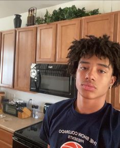 a young man standing in front of a stove top oven next to a kitchen counter